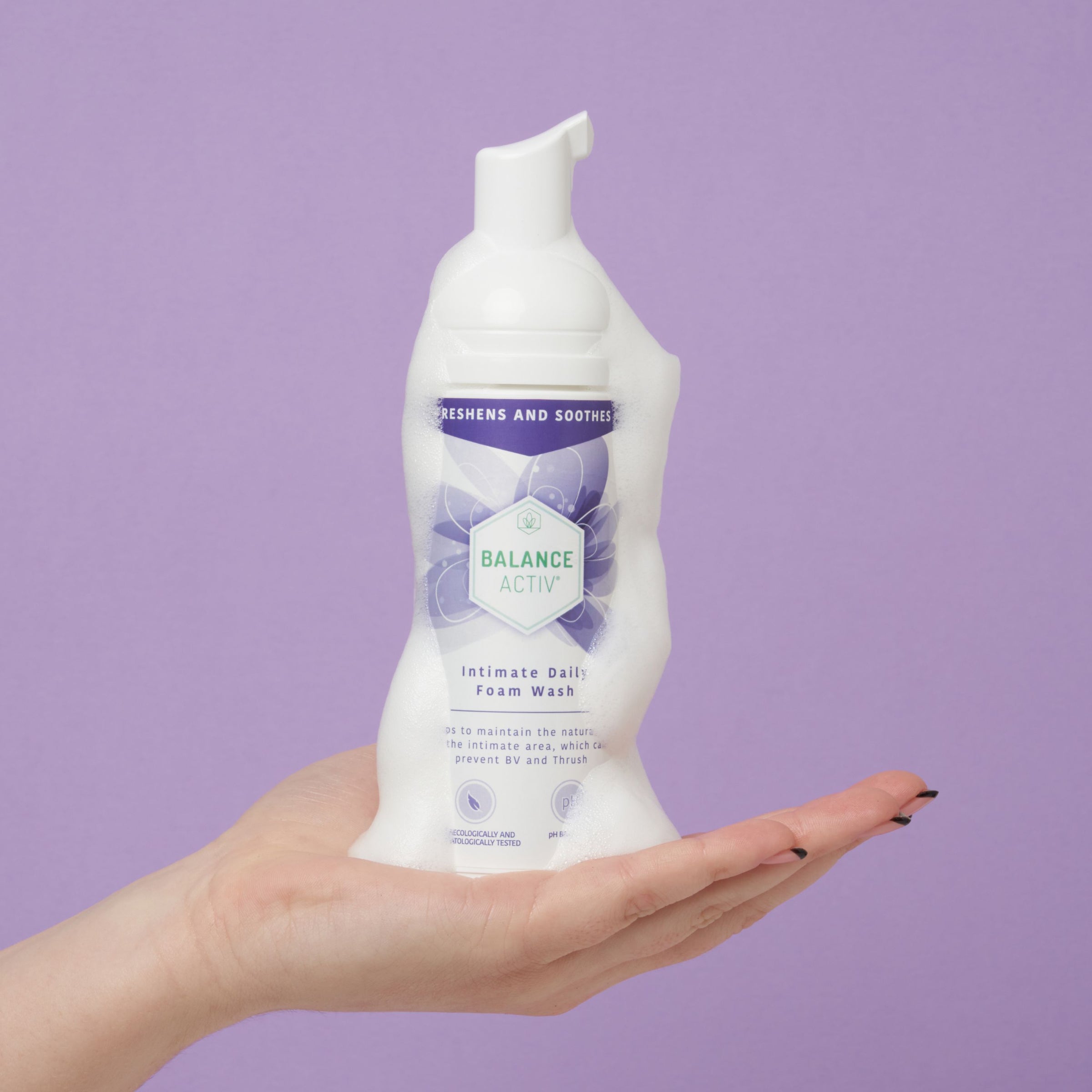 Hand holding a bottle of Balance Activ intimate daily foam wash against a purple background